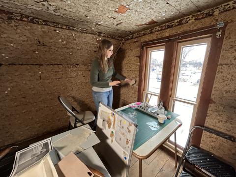 Conservator in the attic bedroom holds a piece of toned paper up against the existing wallpaper.