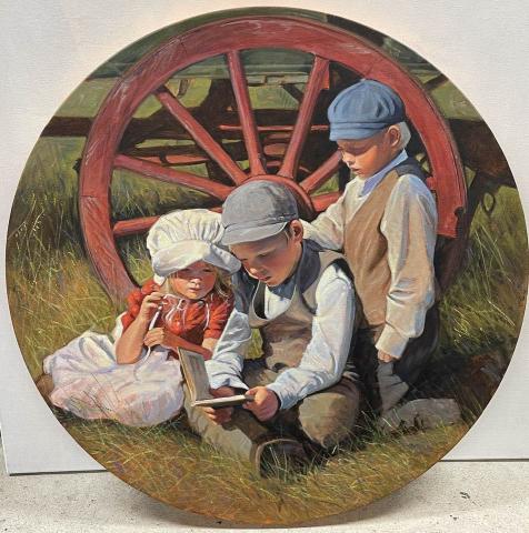 Three children in historic costumes read in front of wagon wheel